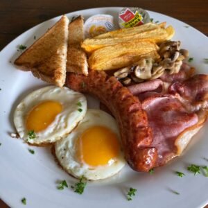 Meat Feast Breakfast — Two eggs, crispy bacon, juicy sausage, golden chips, mushrooms & toast with spreads.
